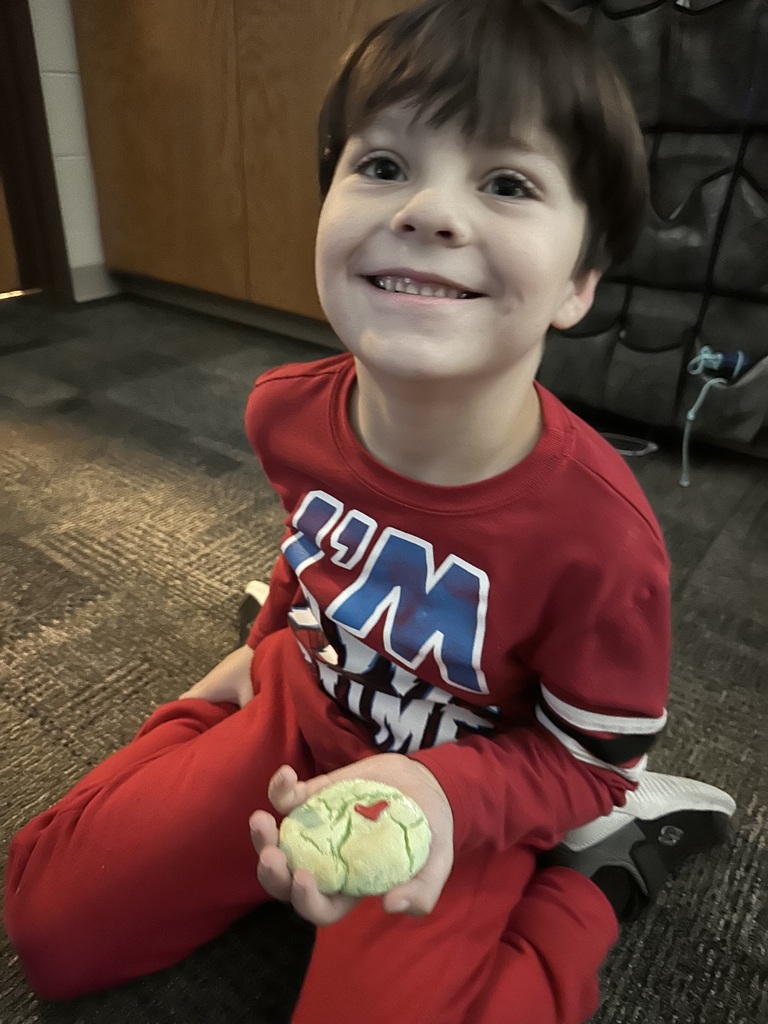 a student smiling while holding a green cookie with a red heart
