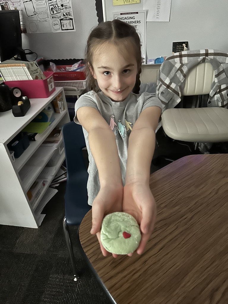 a student holds a green cookie in front of her