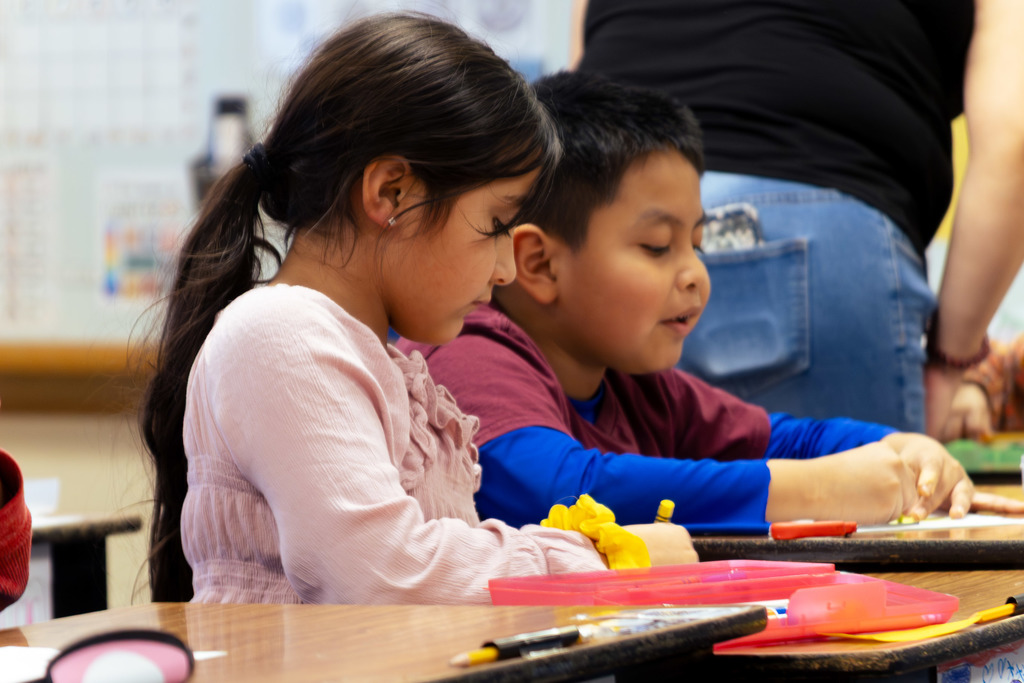 a male and female student coloring an assignment at their desks
