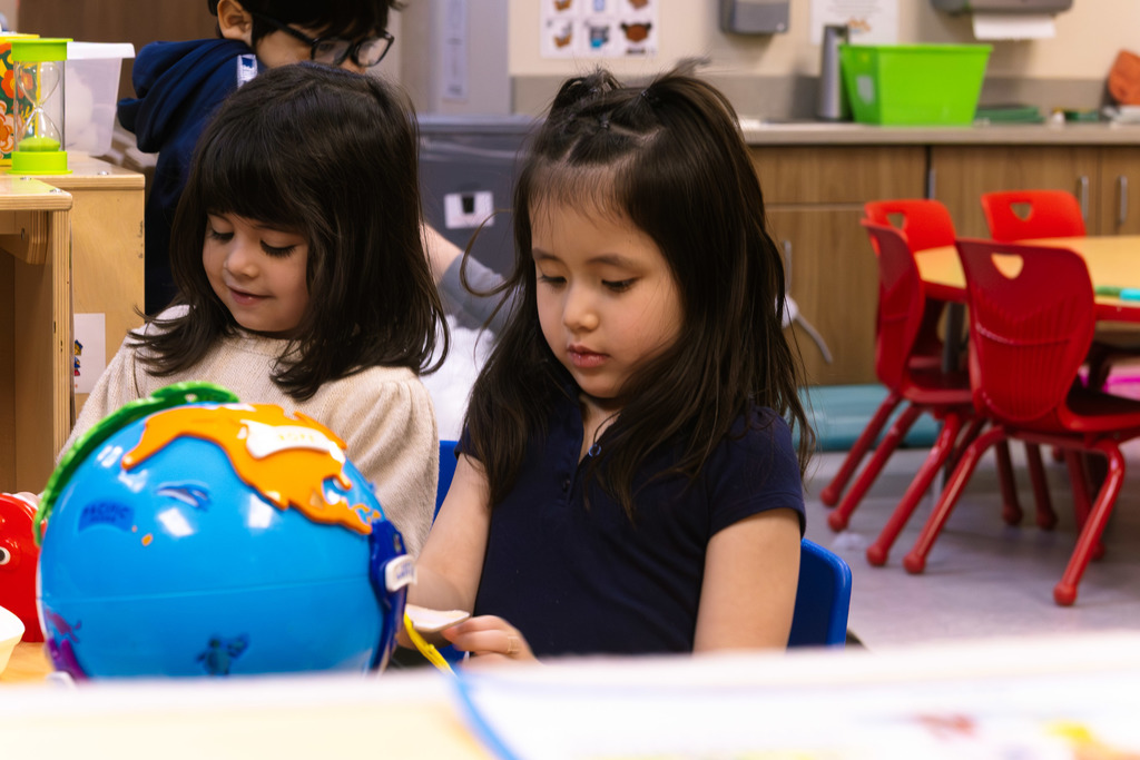 two female students shown playing and learning with a globe