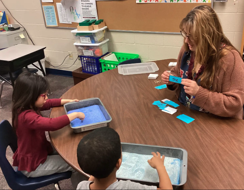Mrs. Peterson and kindergarteners writing letters/words in sand