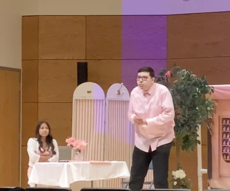 male and female student performing a play. female sitting at a table and male standing, 