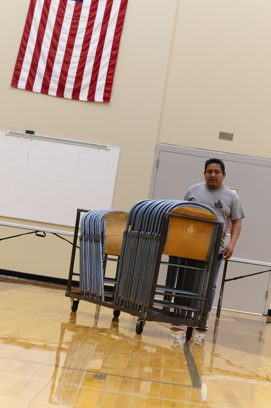 A CHS employee rolls a cart of folding chairs across the gym floor in preparation for a event.