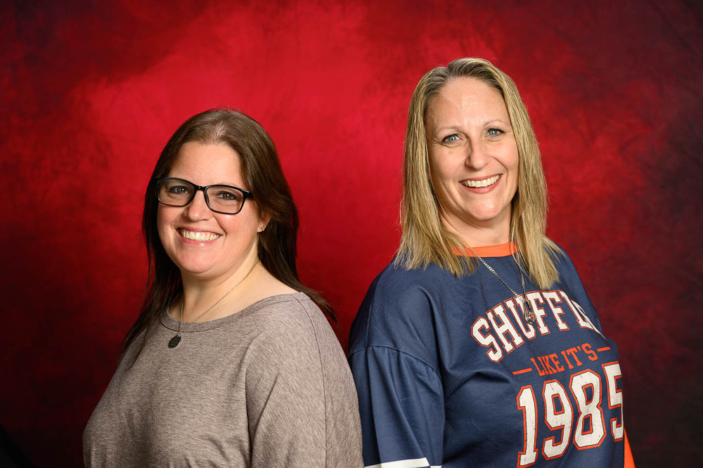 Sarah Lingle and Kathy Costello back to back in front of red backdrop