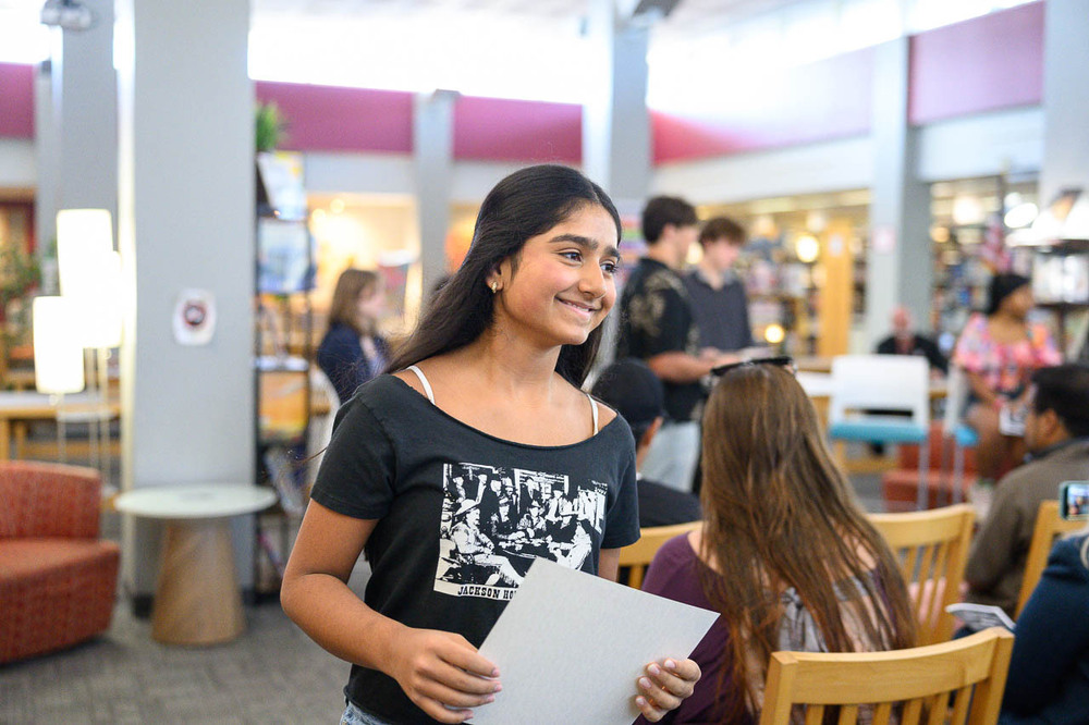 In ILC, student passes camera, holding certificate of NEHS membership