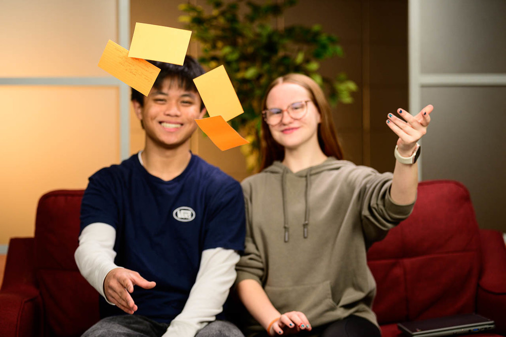 Two out of focus students behind some notecards that they have thrown in the air.