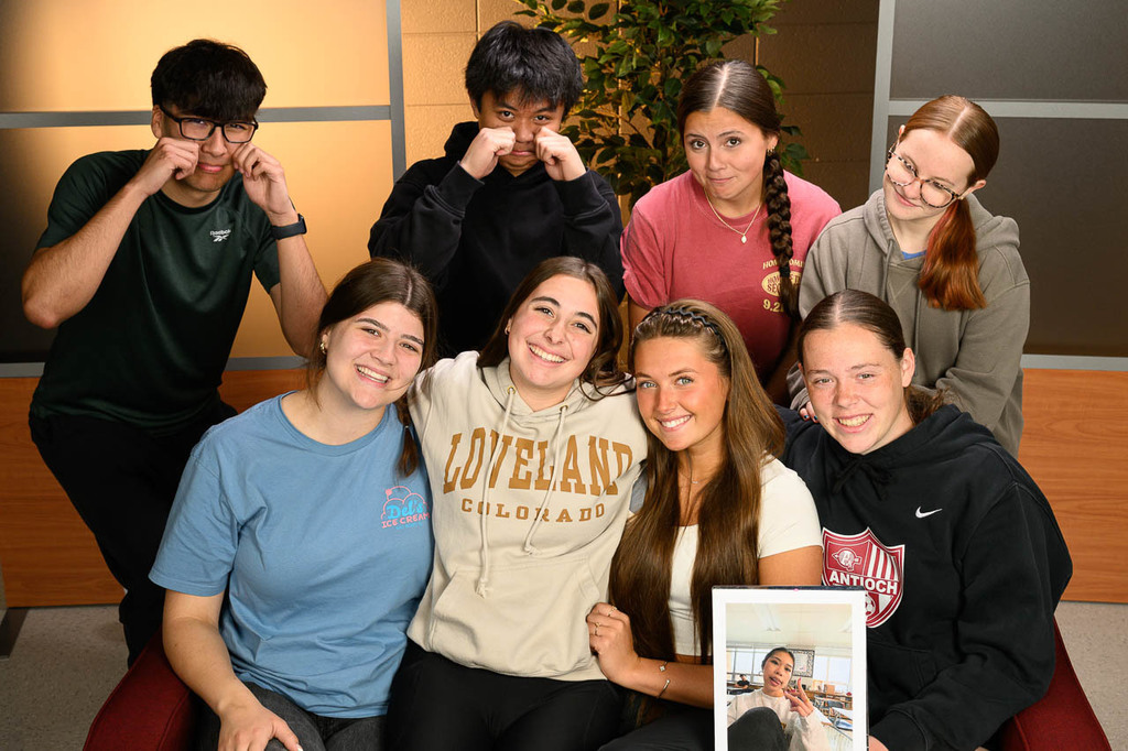 8 students crowd arounc a couch. Seniors in front smile, while underclassmen behind them cry.