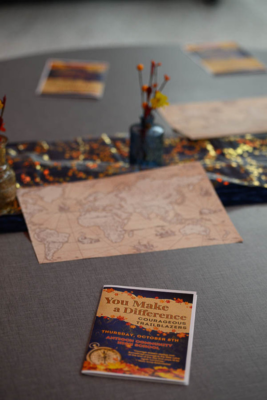 A decorated table set up with placemats, centerpieces, and a "You Make a Difference" program flyer for an event.