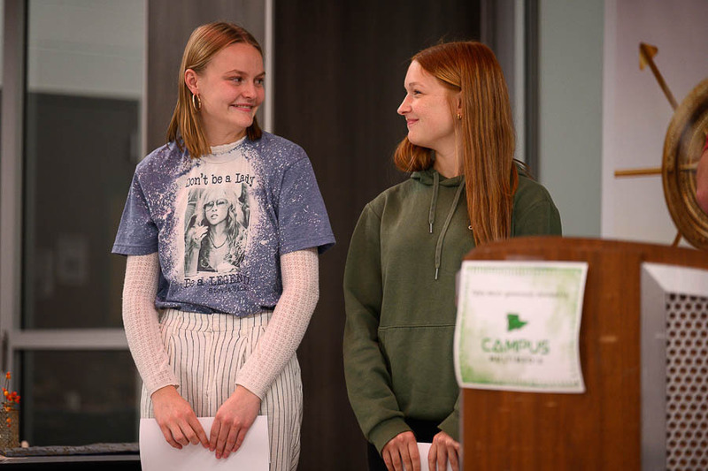 Two smiling female students standing side-by-side next to a podium during a school recognition event.