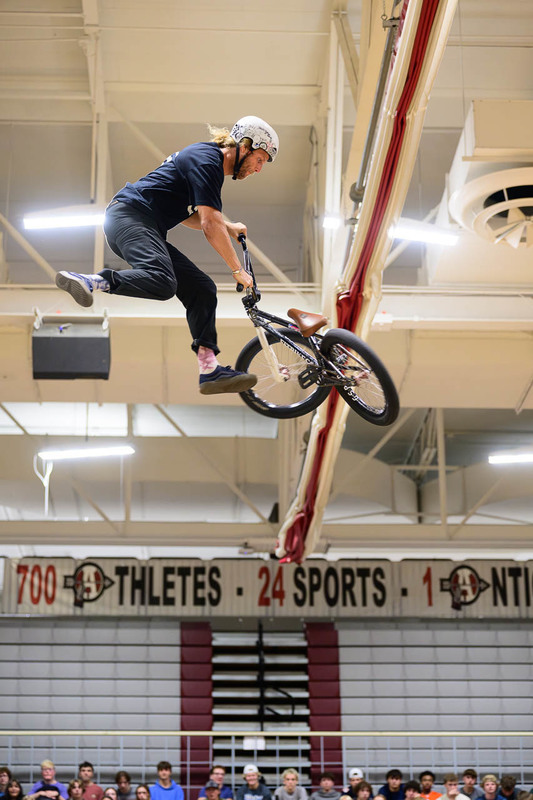 BMX rider airborne with bike tilted, legs extended, Antioch sports banner in background.