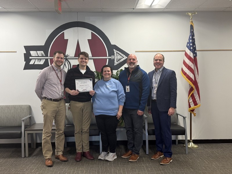 Group of 6 people awarding a certificate to a man in burgandy shirt