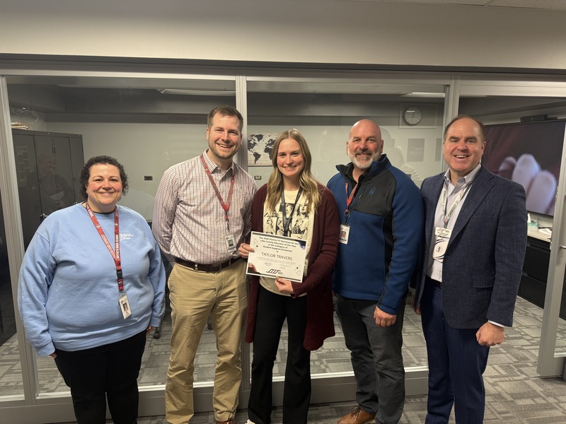 Group of five people awarding a woman in a cardiagan a certificate