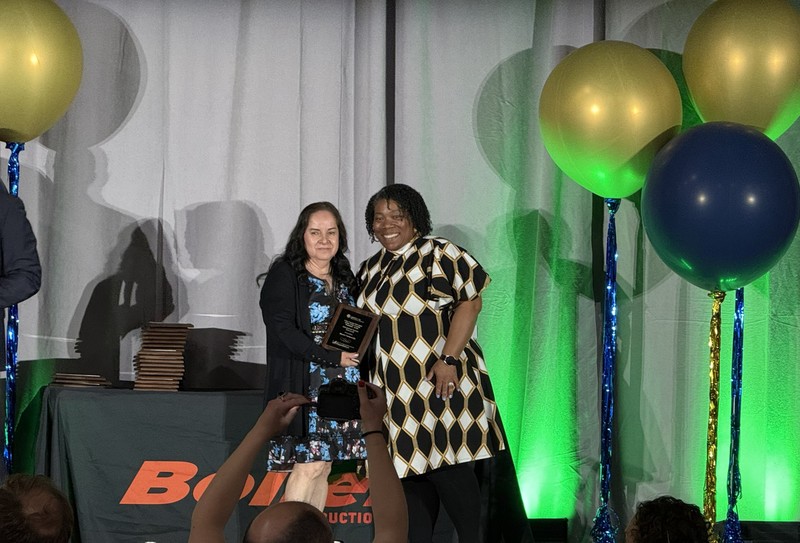 Two women in dresses, one receiving an award