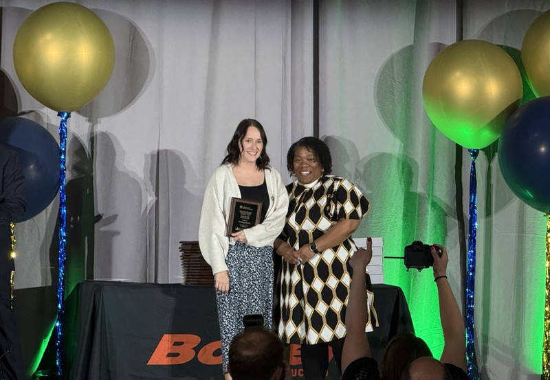 Two women in dresses, one receiving an award