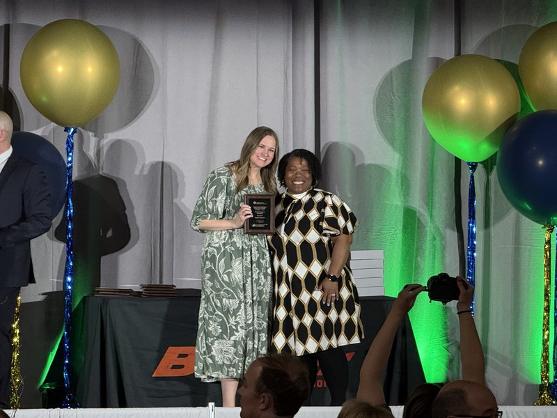 Two women in dresses, one receiving an award