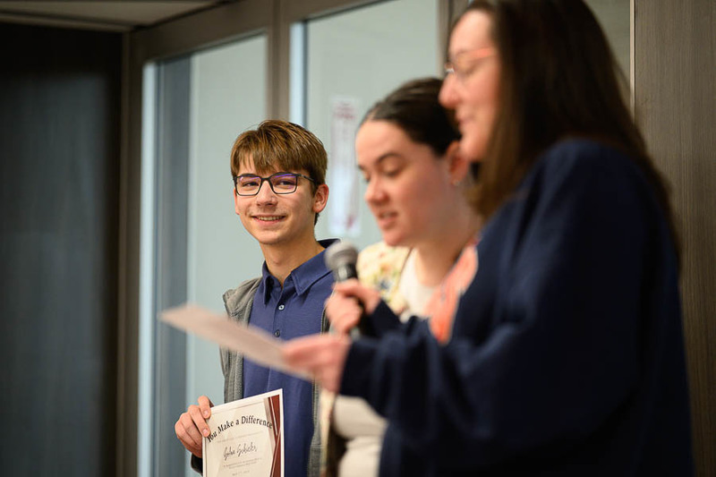 Student smiles with award while two teachers speak