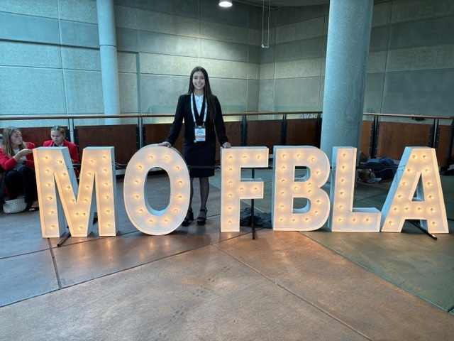 Natali stands behind a lit sign MO FBLA sign.