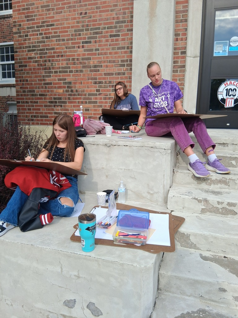 Students sit on steps outside a building creating artwork.