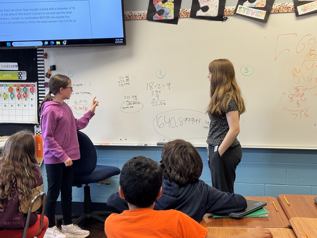 Students solve math equations on a white board in a classroom.