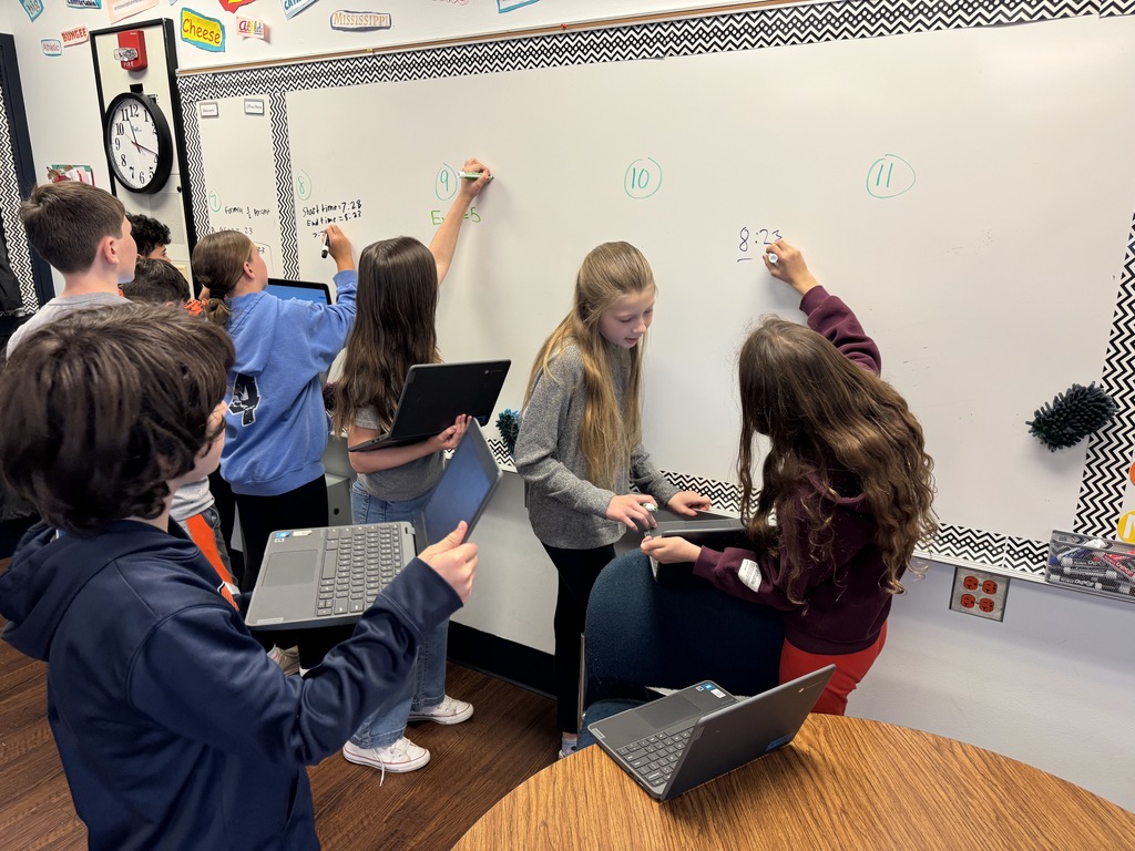 A student solves a math equation on a white board in a classroom.