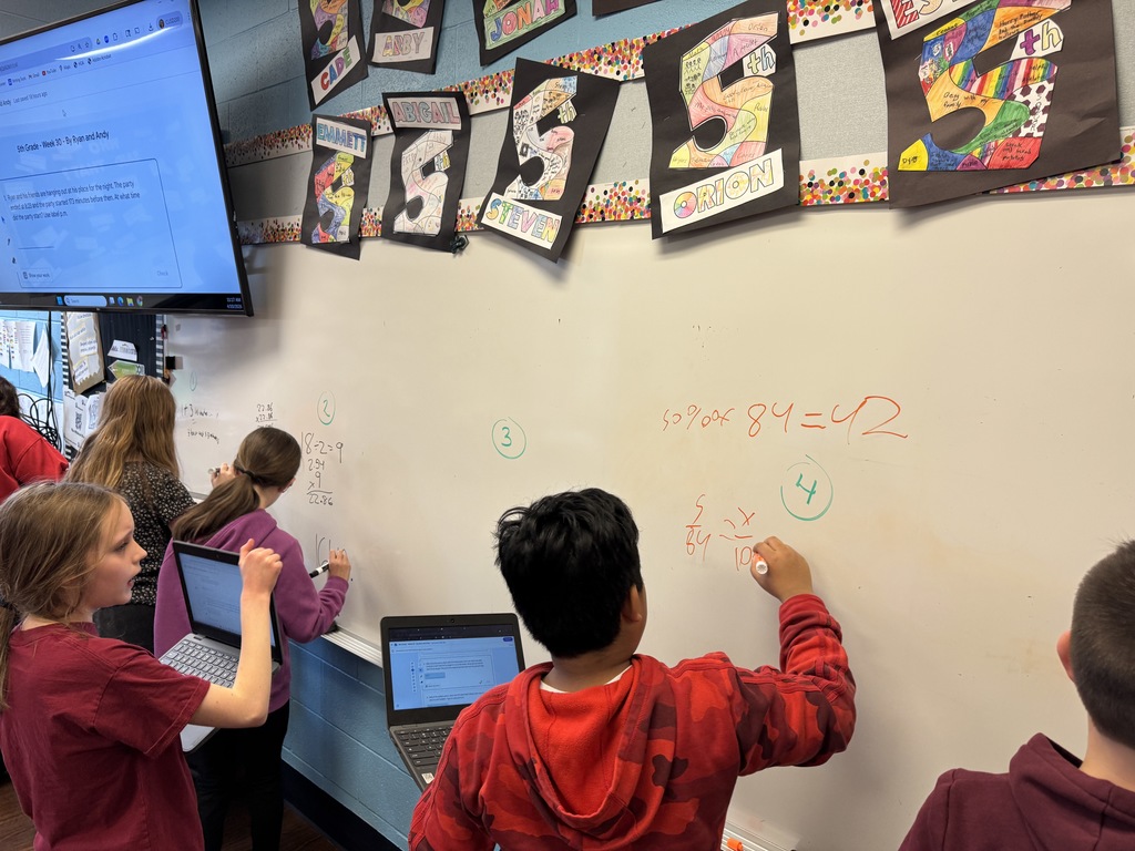 A student solves a math equation on a white board in a classroom.