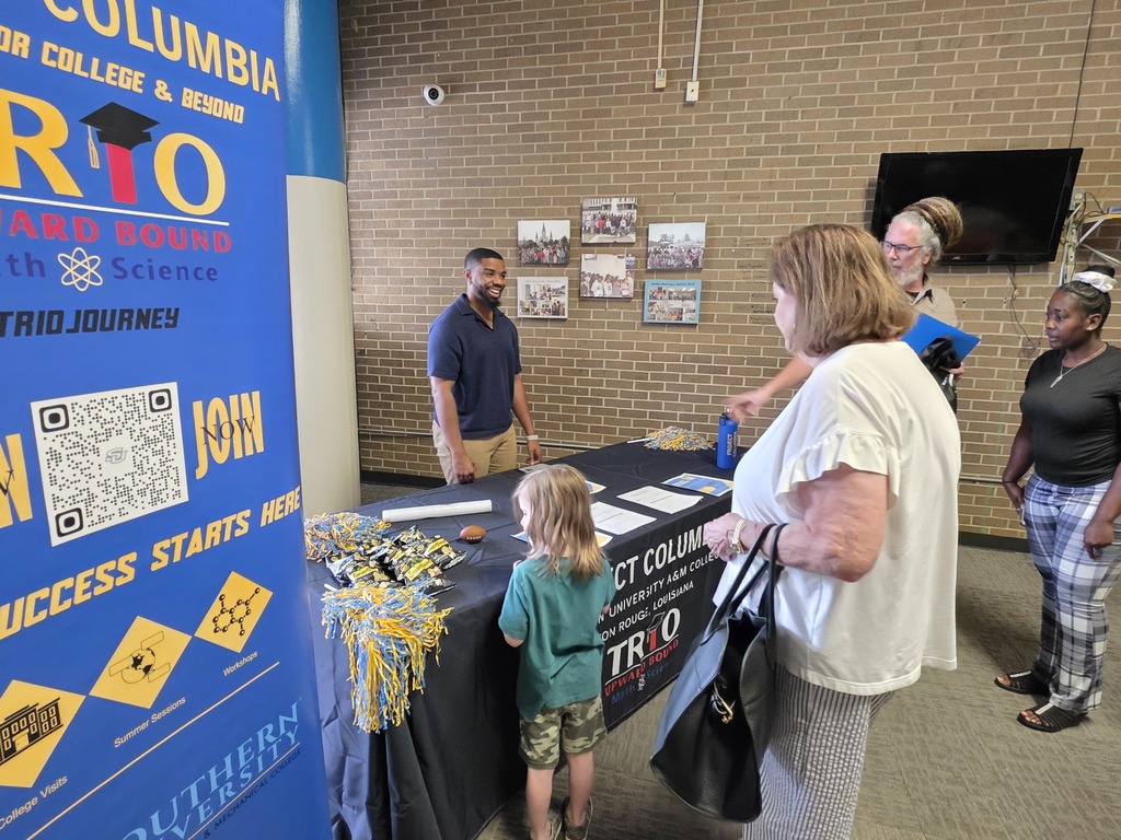 People at a booth, one woman holding a book, a young child in front of a table, and a sign that says "Join" and "Success starts here".