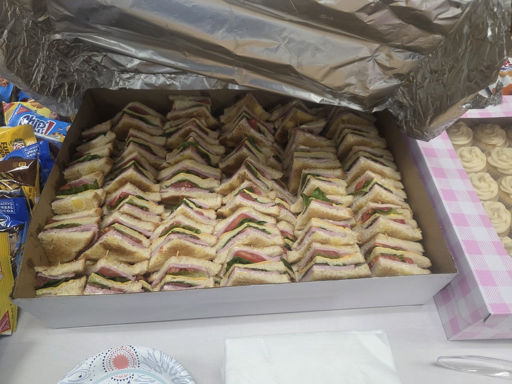 A box filled with many sandwiches, aluminum foil on top. Beside it are more boxes and items.