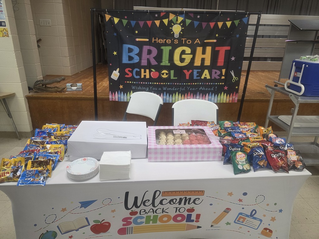A table with snacks, boxes, and a banner reading "Here's To A Bright School Year!" and "Welcome Back To School!"