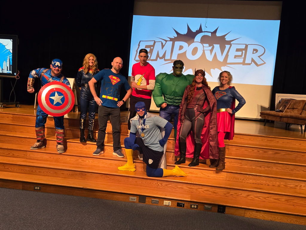Teachers dressed as superheroes on steps at a stage