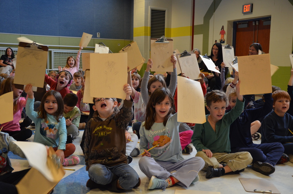 a group of students holding up their artwork during an assembly