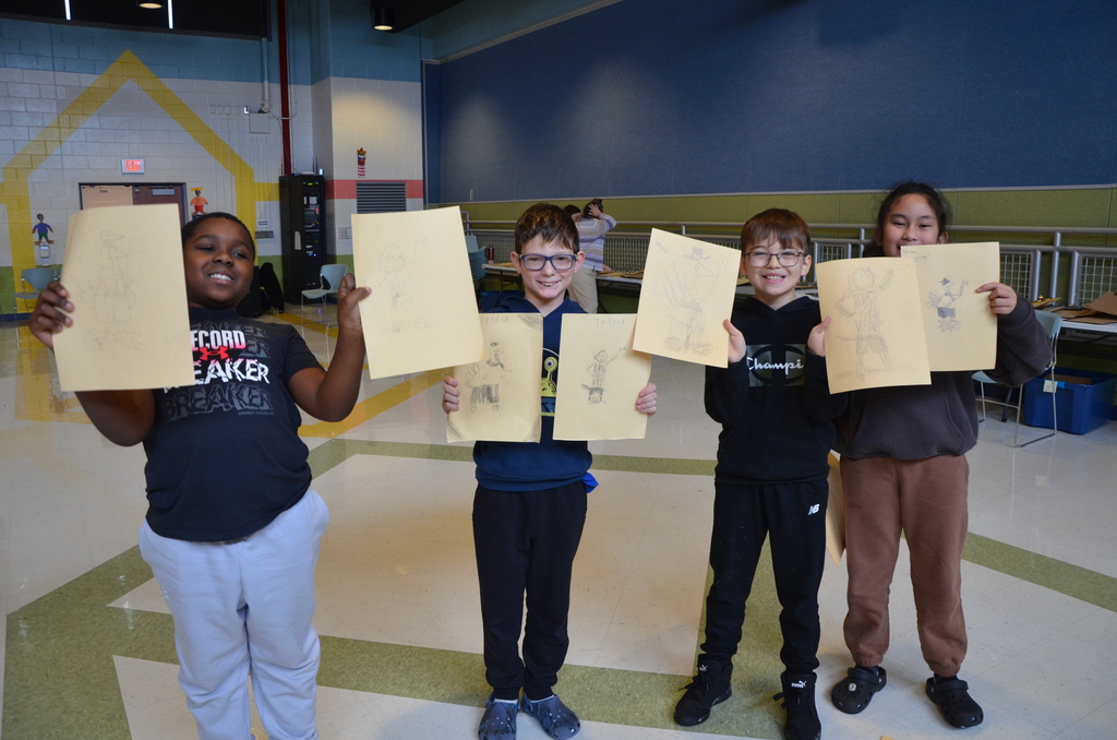 4 students holding up their illustrations from the assembly with Lee Harper