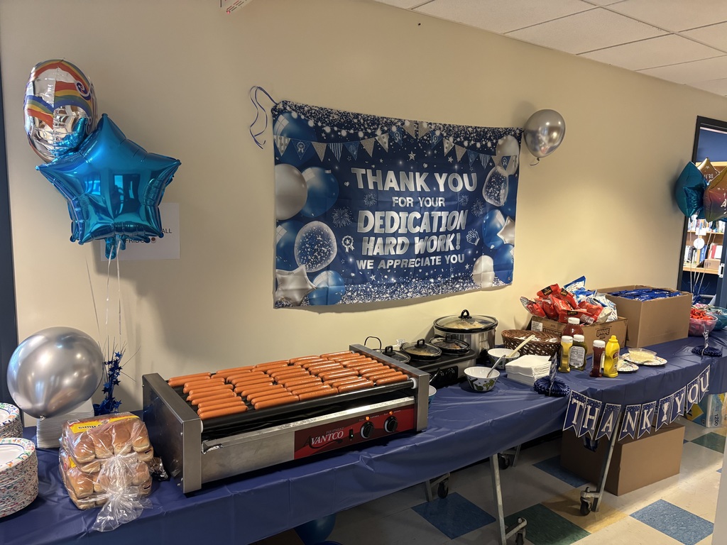 A table with a blue tablecloth that contains hotdogs and snacks 