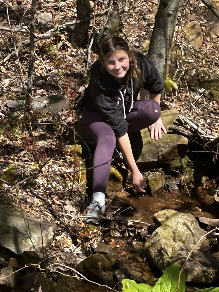 student in the woods near a stream
