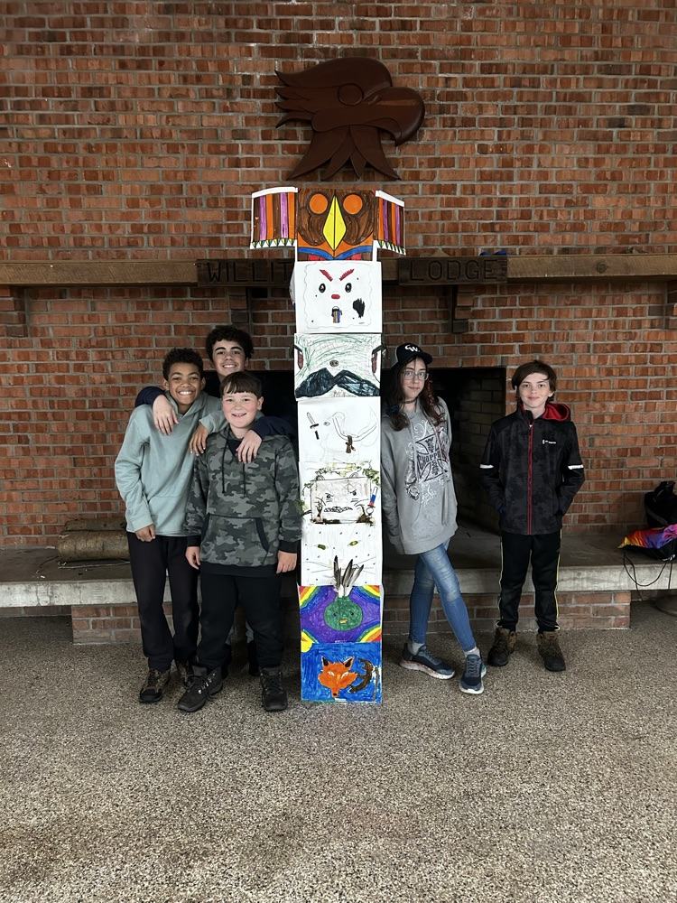 students pose with a totem pole created by camper
