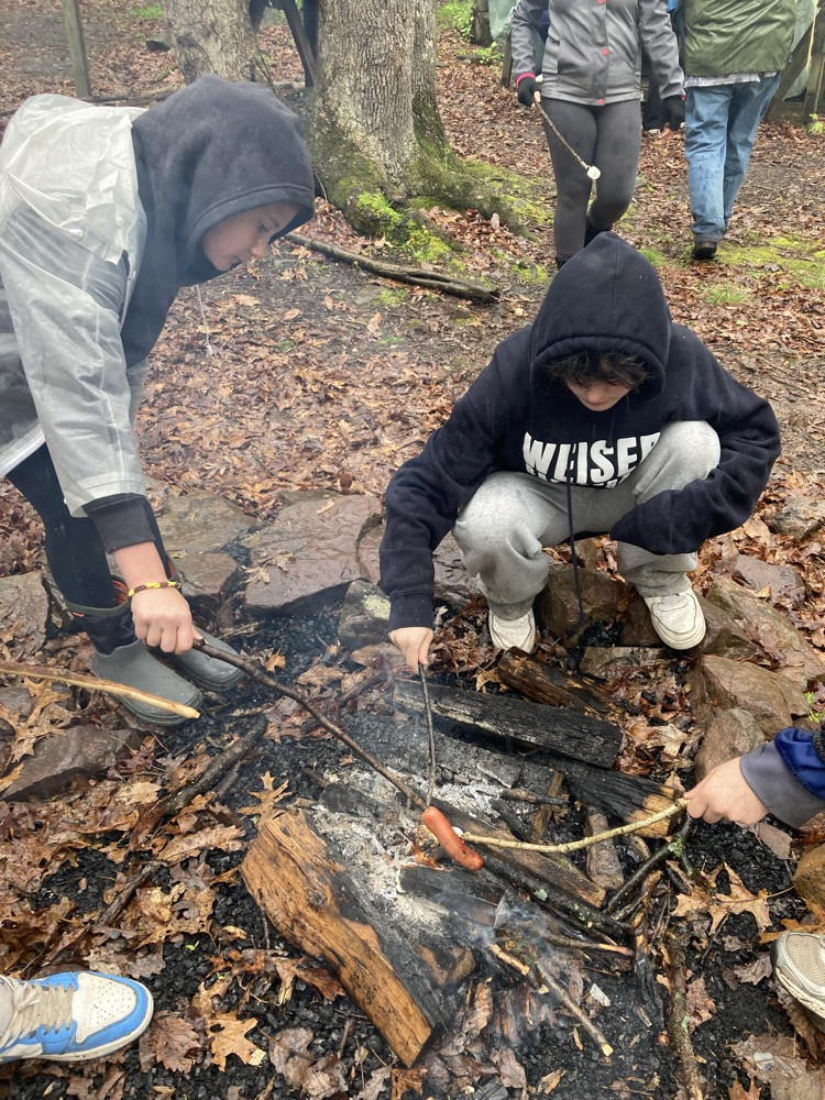 students cooking hot dogs over a fire