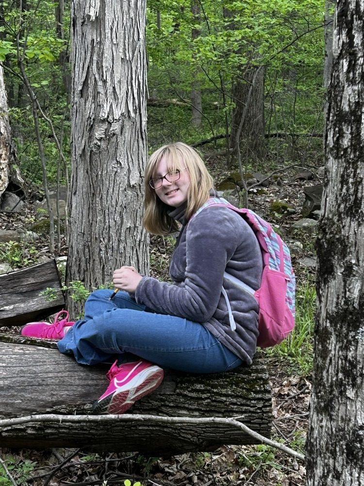 student with pink backpack sitting on a log
