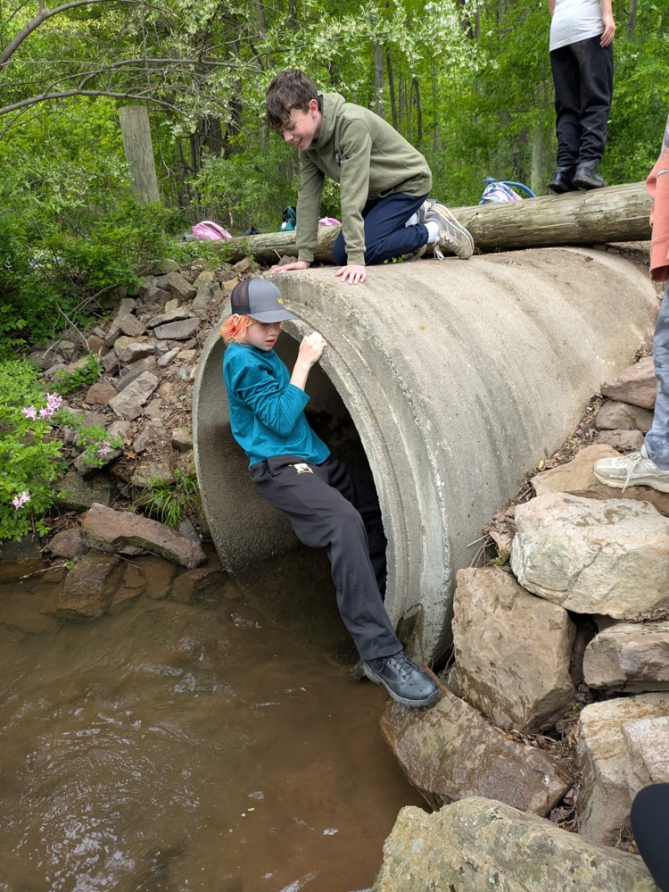 one student kneeling on a concrete tube while another exits
