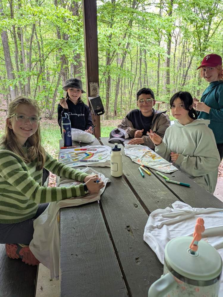 students working on white tshirts sitting at a picnic table