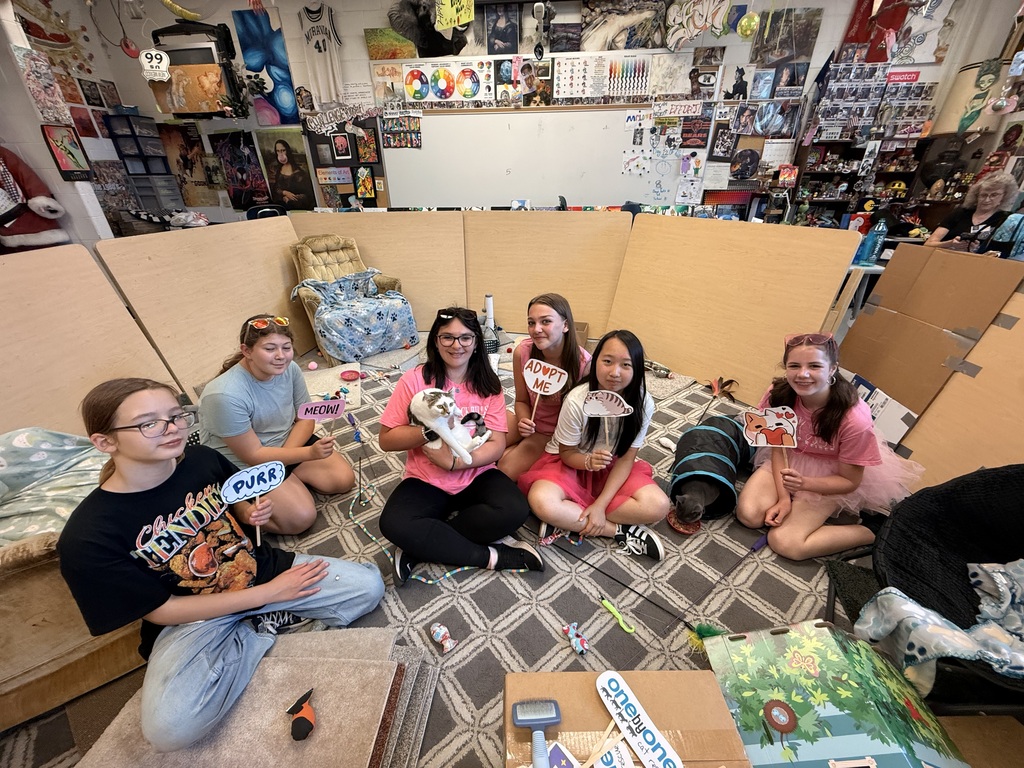 students sitting on a carpet holding signs with cats