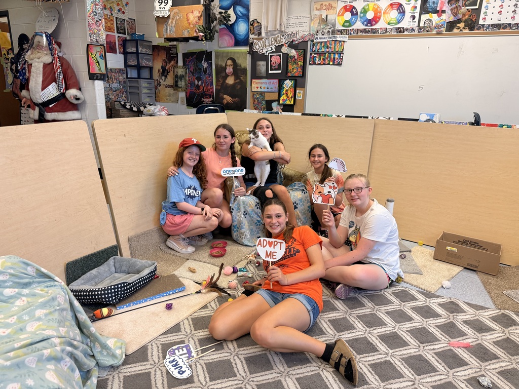 students sitting on a carpet holding signs with cats