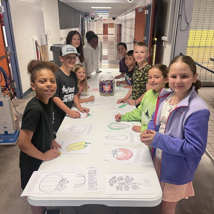 students standing by the pictures they colored to label the raised beds