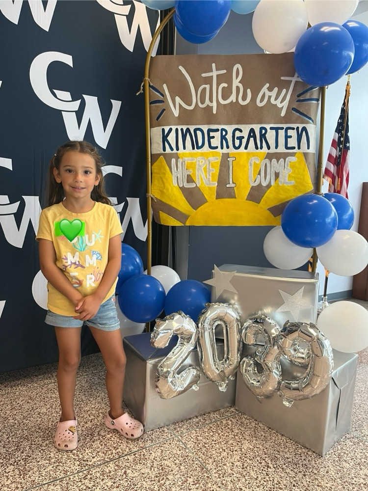 student posing with kindergarten sign