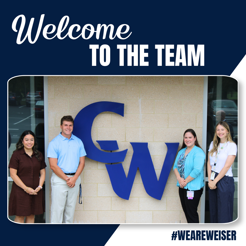 group photo of new teachers next to a large blue CW