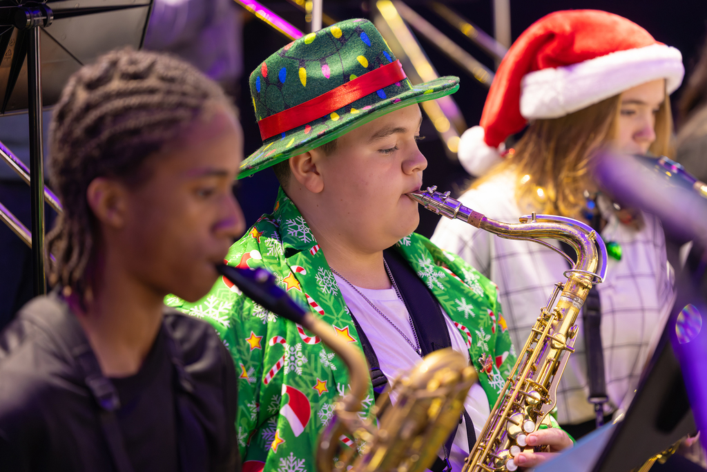 A student in a green holiday suit and hat plays the saxophone.