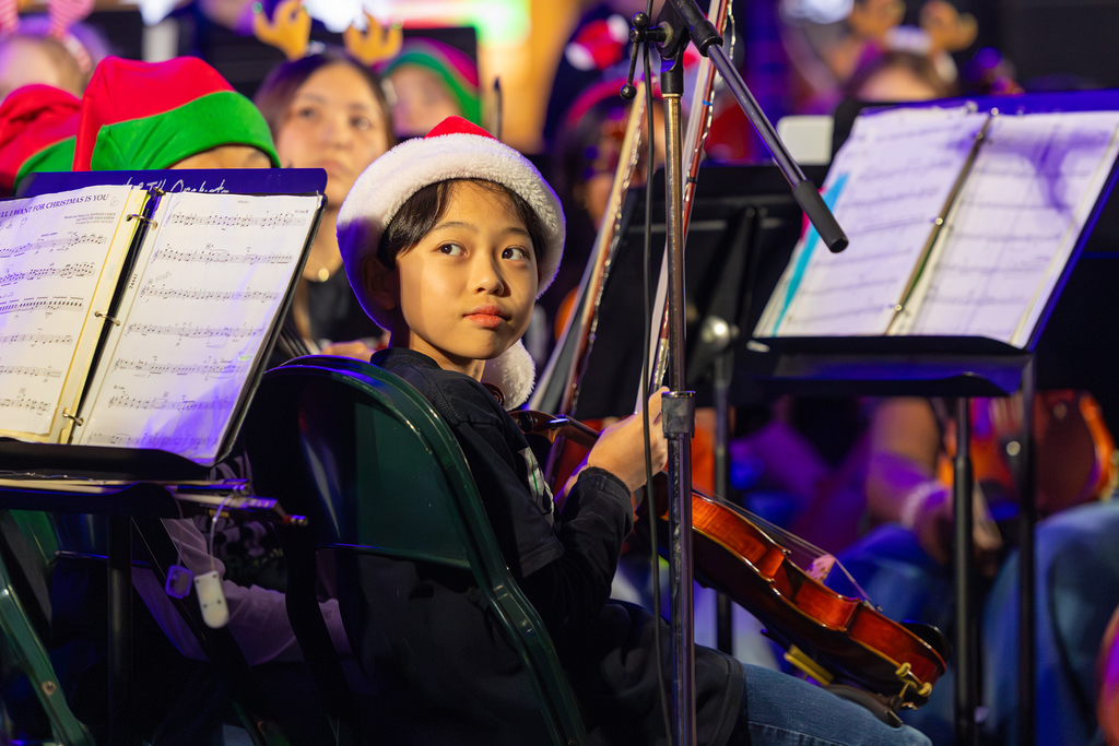 A student wearing a Santa hat looks over their should while holding a violin.