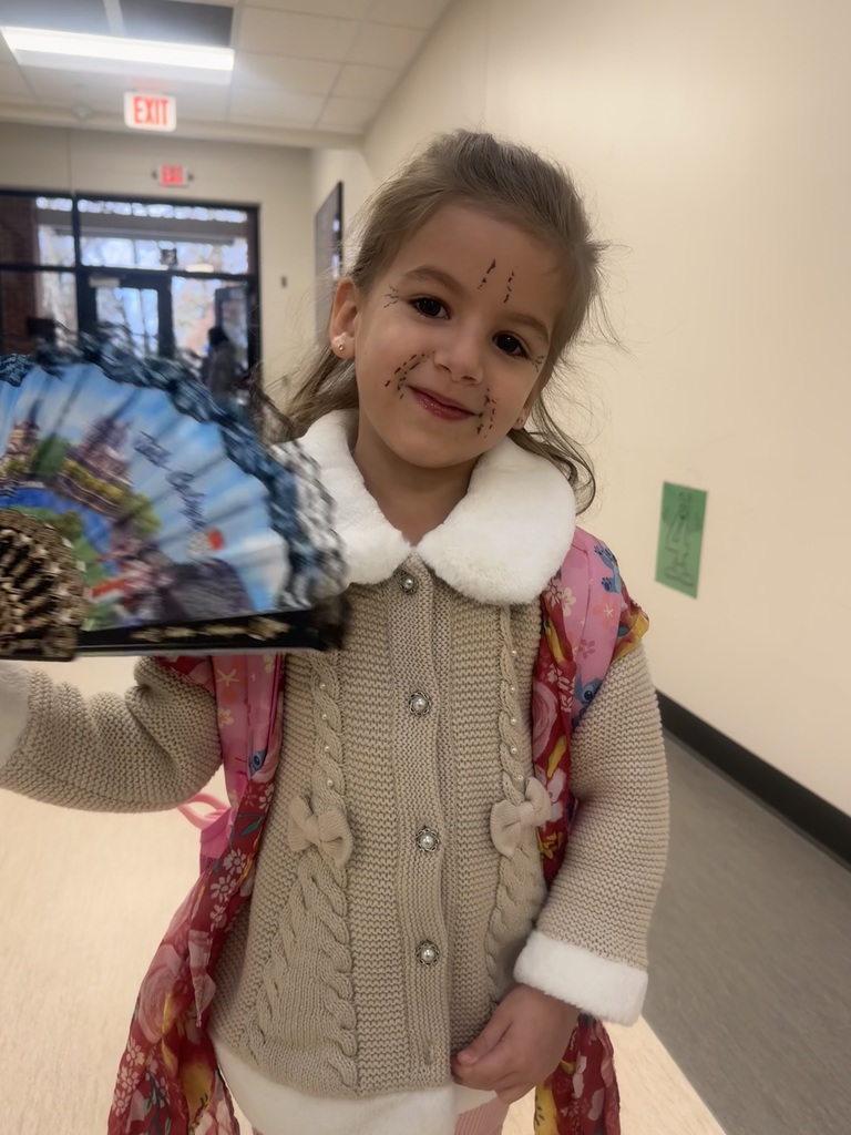 An elementary student using an old-fashioned handheld fan to pose for the picture.