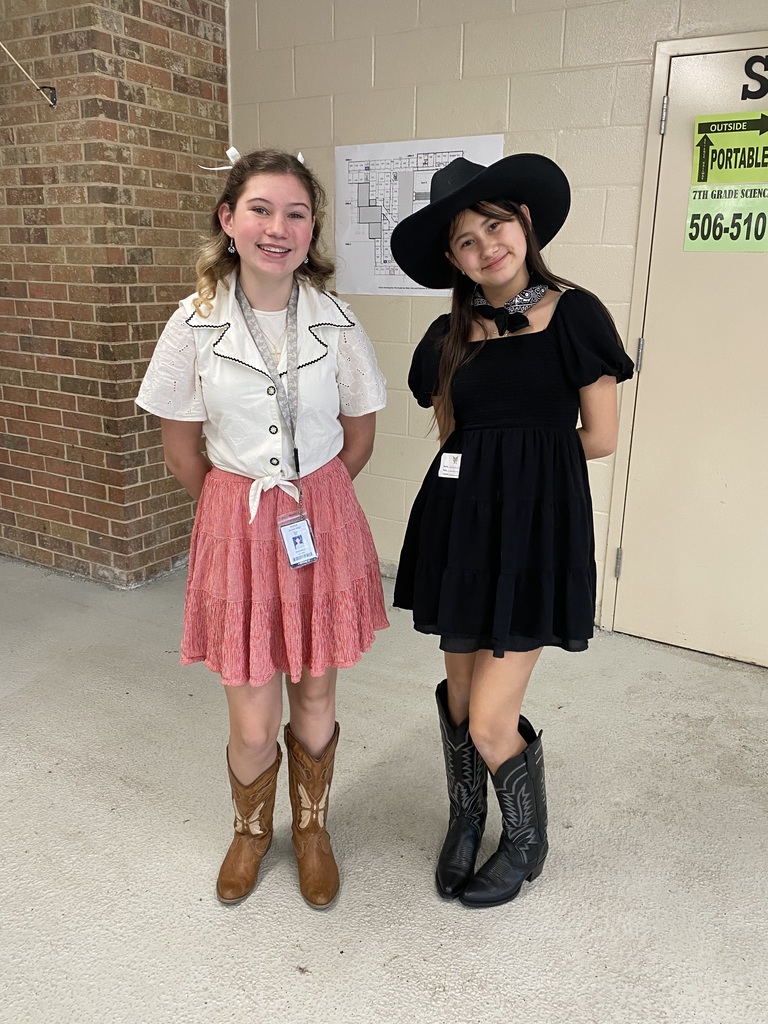 Two students in western attire by a brick wall.