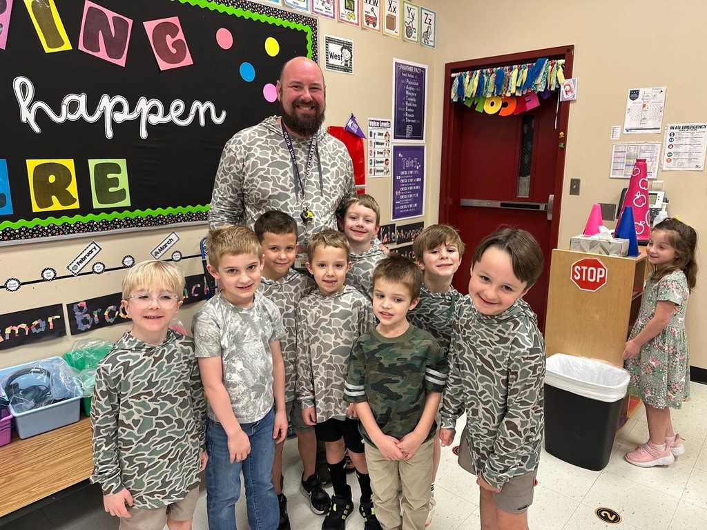 One adult male stands with several students; everyone is in matching clothes and smiling brightly.