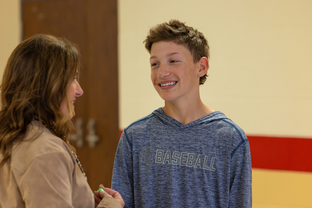 Student smiles while talking with Board member in school hallway.