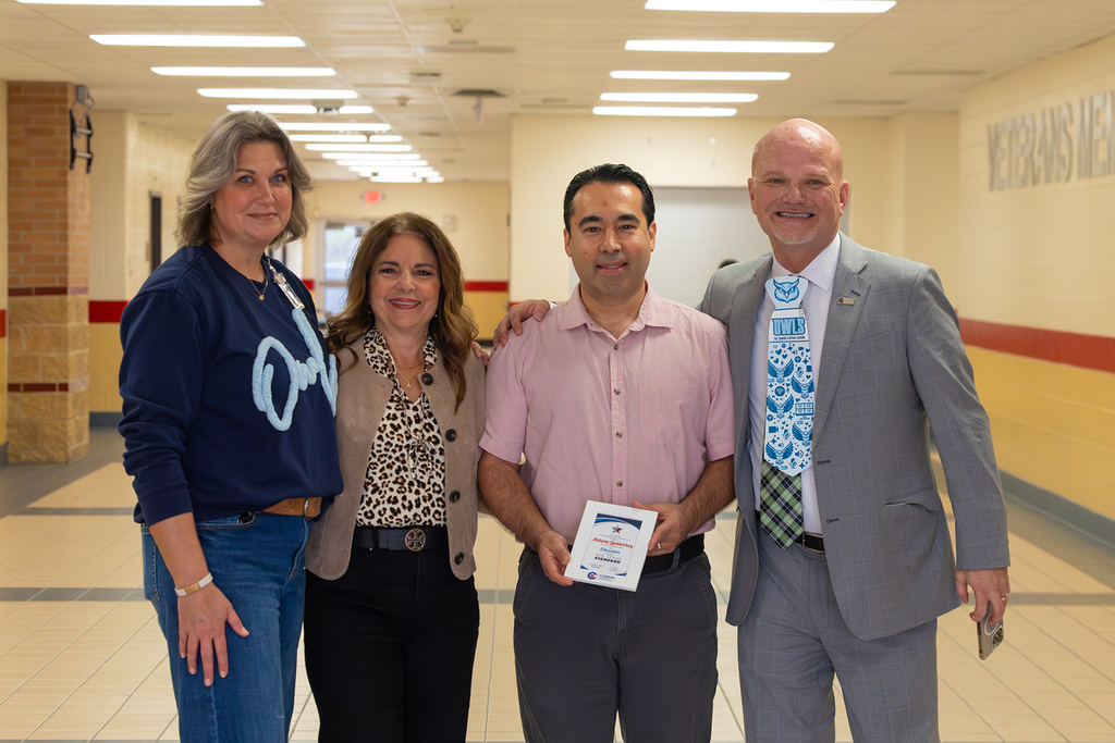 Principal, board member, and superintendent pose in hallway with educator holding award.